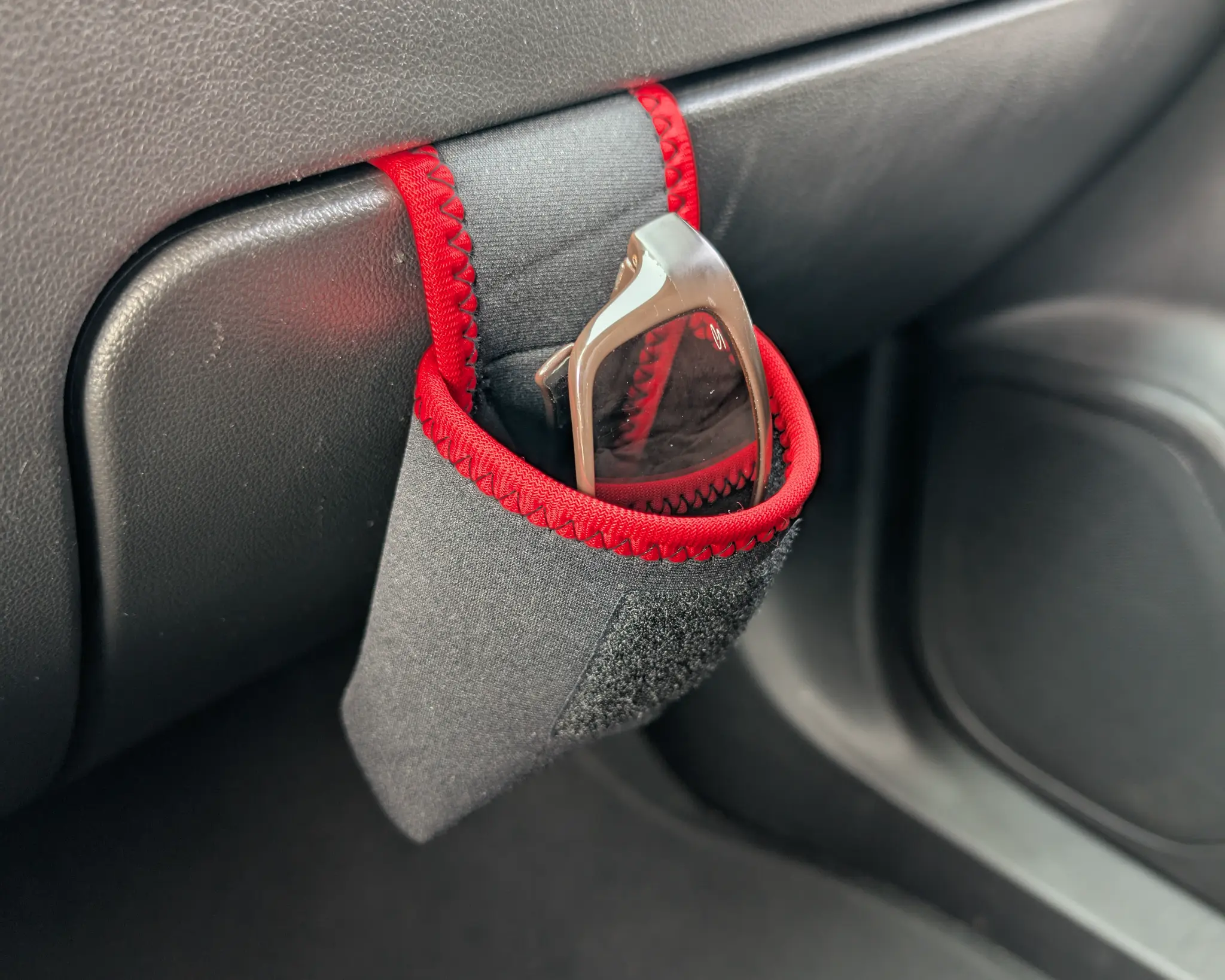 Red ShadeShark mounted on the outside of a glovebox with sunglasses inside